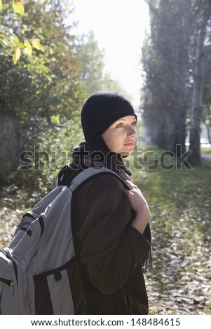 Side view of a beautiful young woman in winter clothing with backpack at park