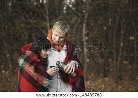 Young couple wrapped in blanket having hot tea in forest