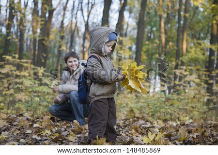 Mother and little son collecting autumnal leaves in park