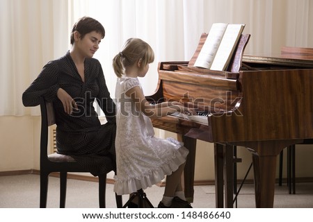 Side view of a girl playing piano accompanied by teacher