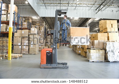 Full length of a man operating forklift truck in distribution warehouse