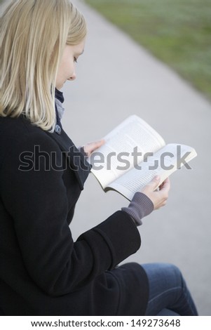 Side view of young blond woman reading book outdoors