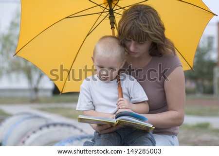 Young woman with son reading book under yellow umbrella in park