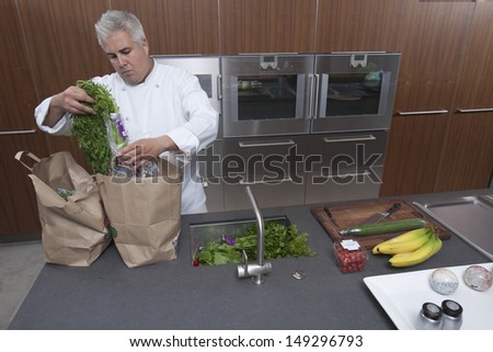 Male chef unpacking groceries from paper bags in commercial kitchen
