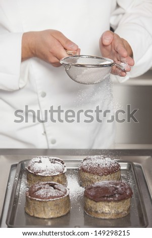 Midsection closeup of male chef icing sugar over chocolate cakes at counter in commercial kitchen