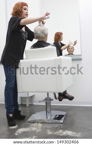 Full length of female hairdresser giving haircut to senior woman in salon