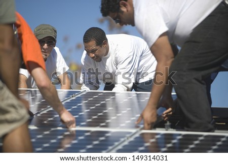 Group of multiethnic engineers placing solar panel on rooftop