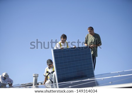 Group of multiethnic workers working on solar panel against clear blue sky