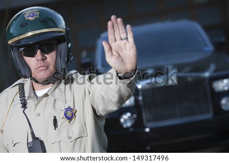 Confident middle aged traffic cop signaling stop gesture with car in background