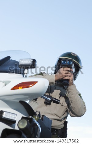 Low angle view of middle aged traffic cop monitoring speed through radar against sky