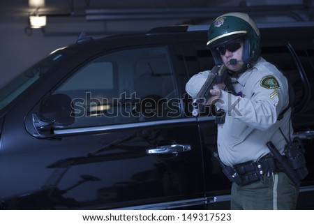 Confident traffic cop aiming rifle while standing against car