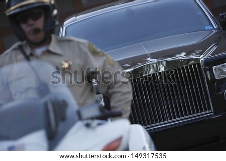 Middle aged traffic cop sitting on motorbike with car in background