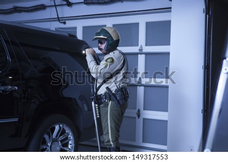 Side view of middle aged policeman with flashlight investigating car in garage