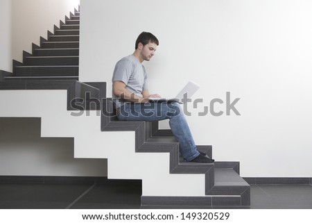 Full length side view of young man using laptop while sitting on steps at home