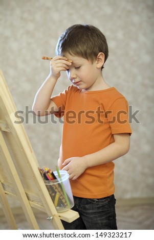 Confused boy with hand on forehead standing in front of easel