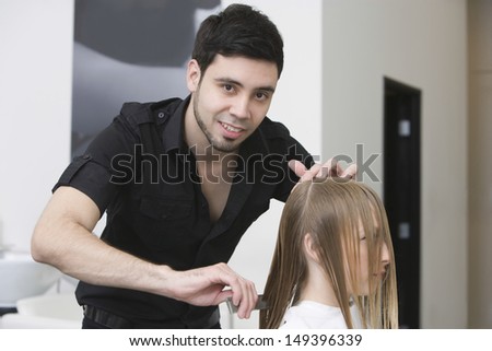 Portrait of male hairstylist combing client\'s hair at beauty salon