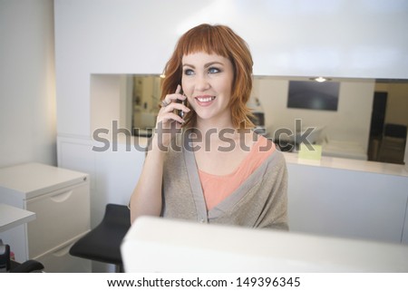 Beautiful young hairdresser answering mobilephone at reception in salon