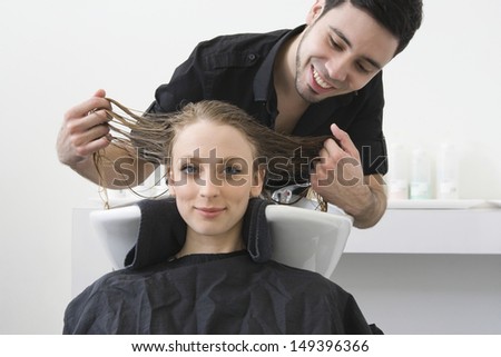 Portrait of beautiful woman smiling with hairstylist examining her hair at beauty salon