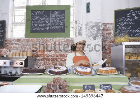 Middle Aged Female Owner Working At Counter In Cake Shop