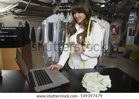 Young female owner calculating amounts on laptop at counter in laundry