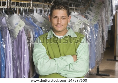 Portrait of happy young man with arms crossed standing in front of clothes rail