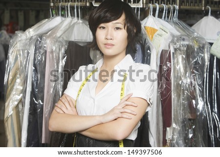Portrait of confident young woman with arms crossed standing against clothes rail in laundry