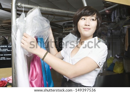 Happy young woman unwrapping plastic from dry cleaned clothes in laundry