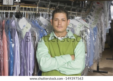 Portrait of young man with arms crossed standing in front of clothes rail