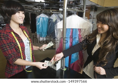 Happy young female customer paying money to laundry owner
