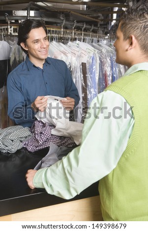 Male laundry owner showing dry cleaned shirts to customer at counter