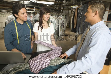 Laundry owners showing dry cleaned clothes to customer at counter in laundry