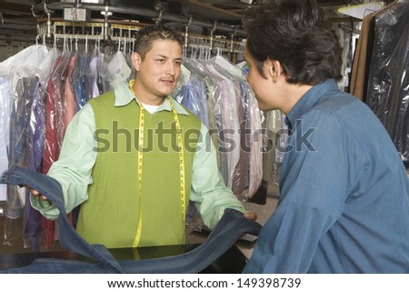 Young male owner showing dry cleaned jeans to customer at counter in laundry