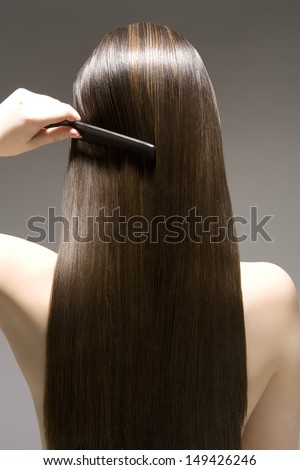 Closeup Rear View Of A Woman Combing Her Long Brown Hair Against Gray Background