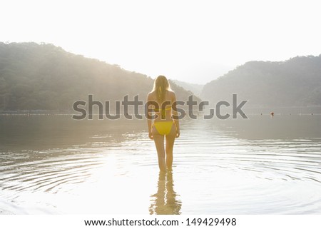 Rear view of a young woman in yellow bikini standing in lake