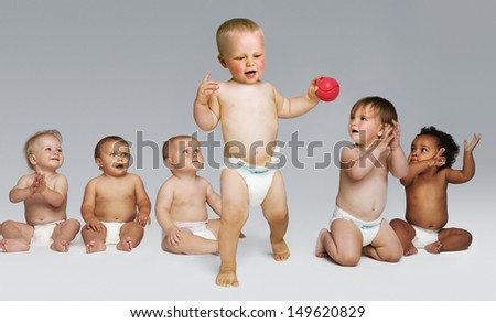 Full length of babies looking at a toddler take first steps against gray background