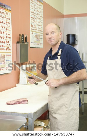 Supermarket employee sharpening knife at meat counter in supermarket