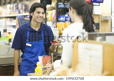 Supermarket employee in blue apron assisting female customer