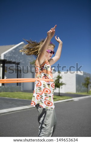 Side view of a young girl playing with plastic hoop outdoors