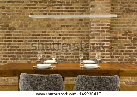 View Of Wineglasses And Plates On Dining Table Against Brick Wall In Modern House