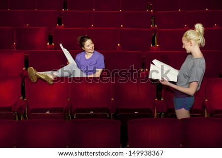 Two young women sitting in theatre stall with scripts