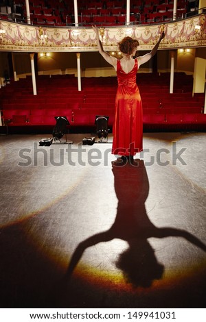 Full Length Rear View Of A Woman In Red Gown Standing On Stage Floor