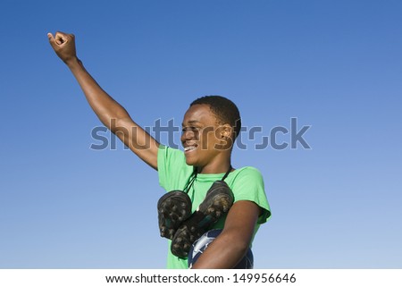 African American man with football boots round his neck and an arm raised against clear blue sky