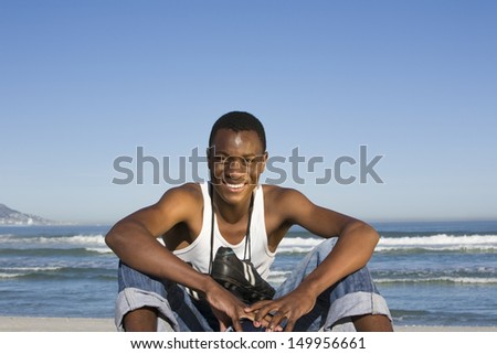 Portrait of a smiling young man with football boots round neck on beach