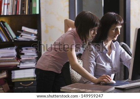 Side view of a mother and daughter looking at computer screen in house