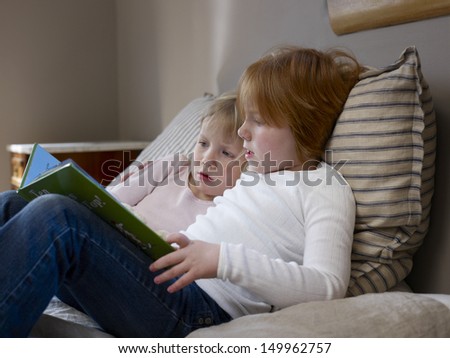Side view of two young sisters reading book on a bed