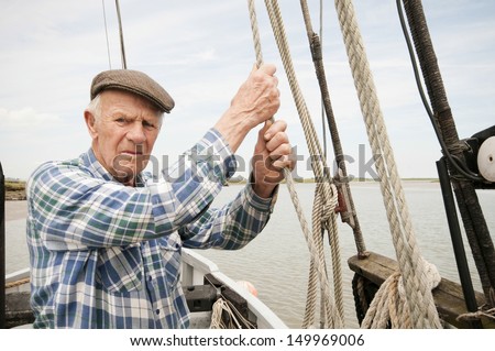 Portrait of a senior fisherman pulling rope on deck of a boat