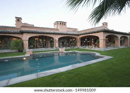 Swimming Pool And Lawn In Front Of Spacious House Against Clear Sky
