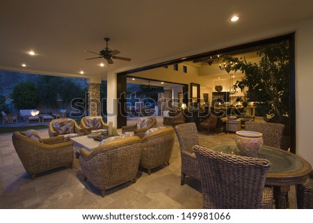 Wicker furniture in lit spacious home with porch view at night