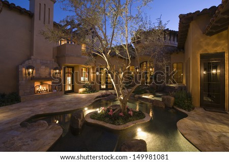 Paved Courtyard With Pond In Lit House Against Clear Sky