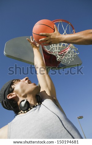 Low angle view of young man playing basketball with friend against blue sky